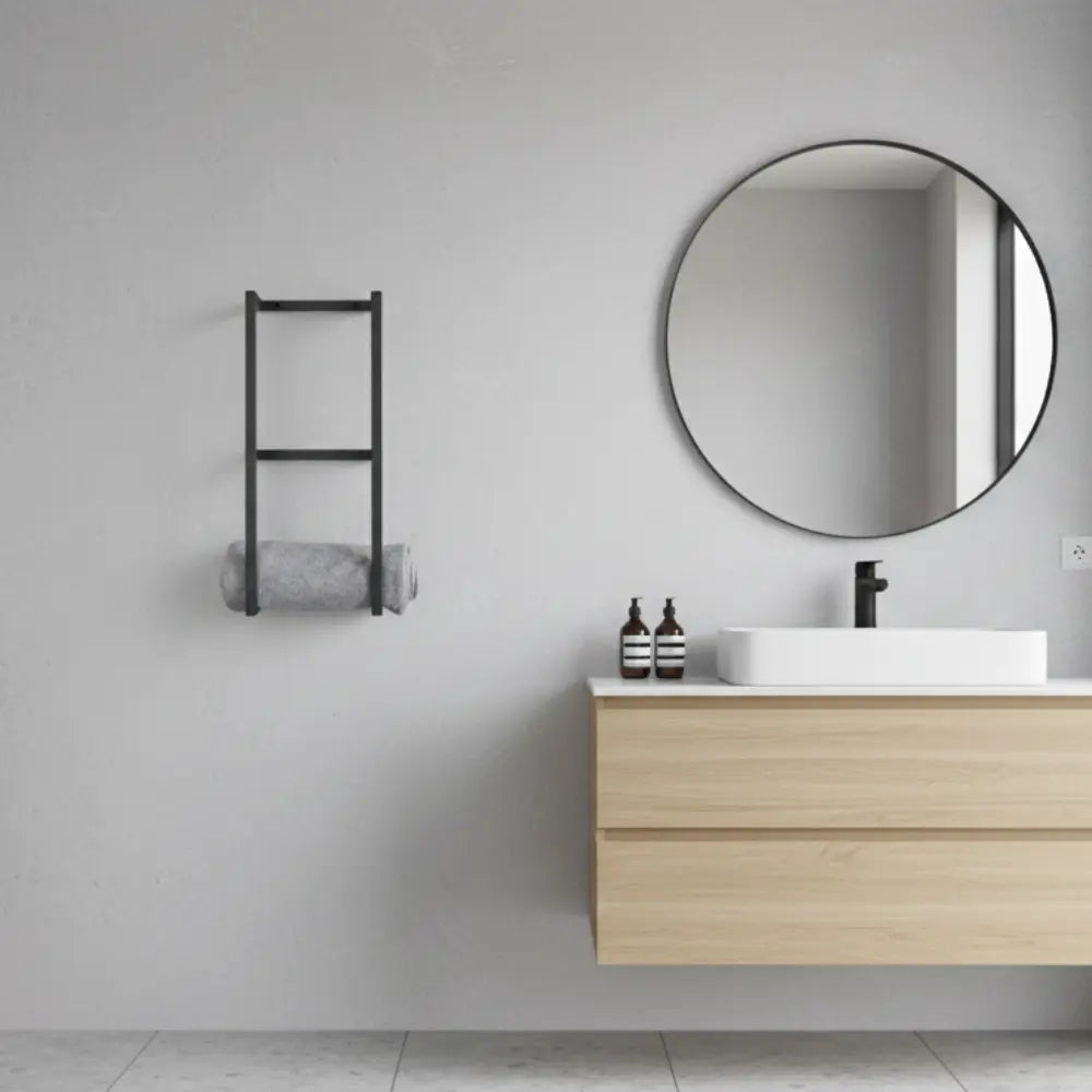 Vue d'ensemble d'une salle de bain épurée avec un meuble vasque en bois, un miroir rond noir et un porte-serviette design fixé au mur.